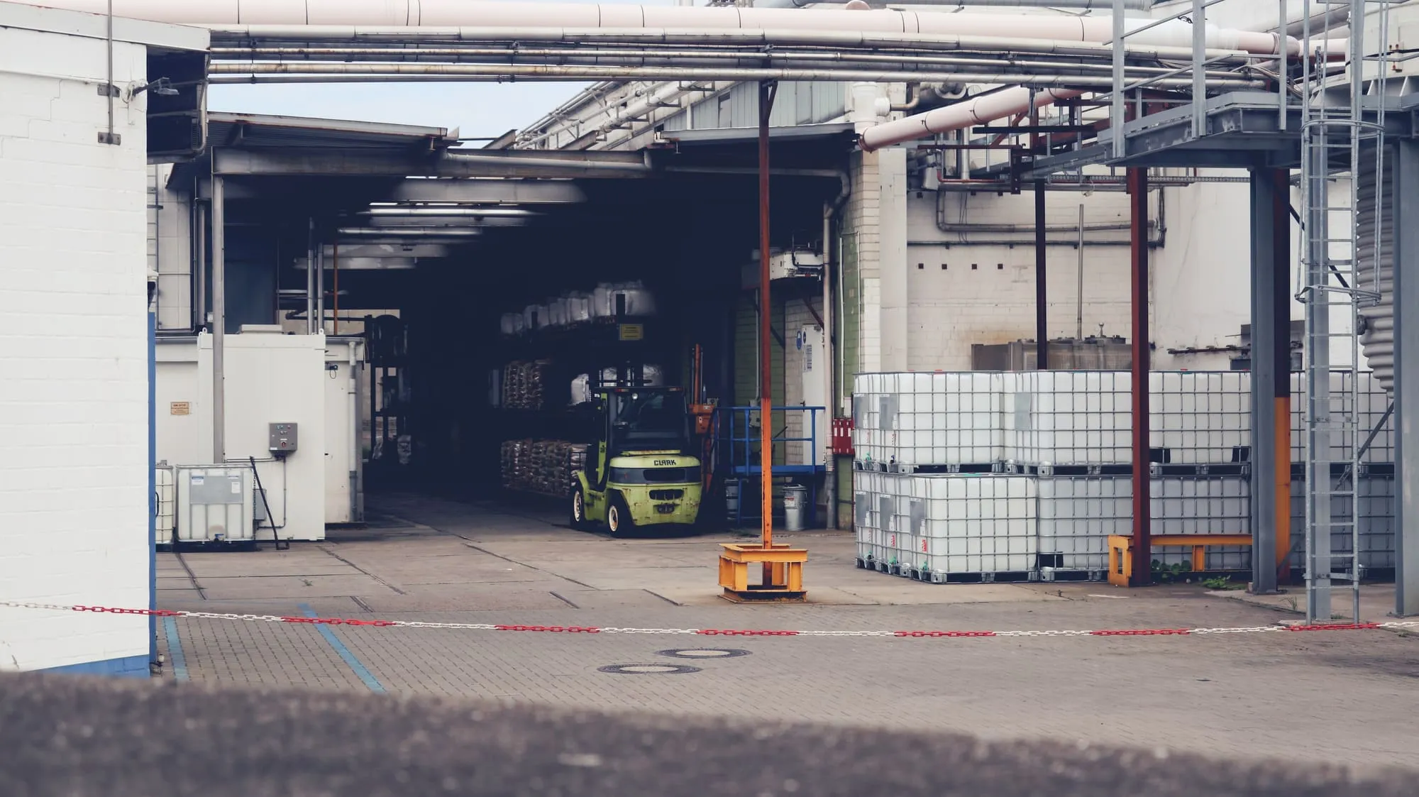 A forklift at a loading dock beside stacked bulk liquid totes