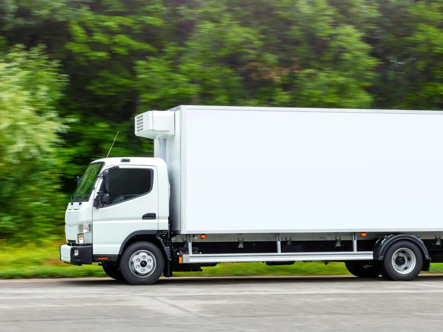White refrigerated box truck driving along a tree-lined road